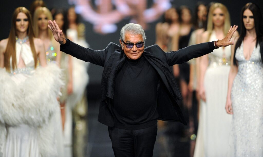 Roberto Cavalli at a fashion event wearing a dark suit and signature sunglasses