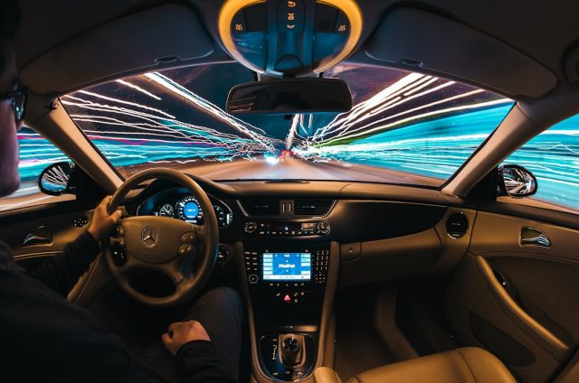 Tesla Robotaxi Launch Plagued by Lane Drifting, Sudden Braking, Unsafe Drop-Offs A Tesla robotaxi with a human safety monitor in the front seat drives on an Austin street, surrounded by traffic and pedestrians.