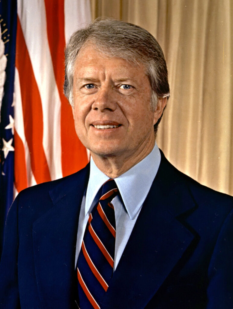 Jimmy Carter smiles at his Plains home, surrounded by family, celebrating his 100th birthday milestone.